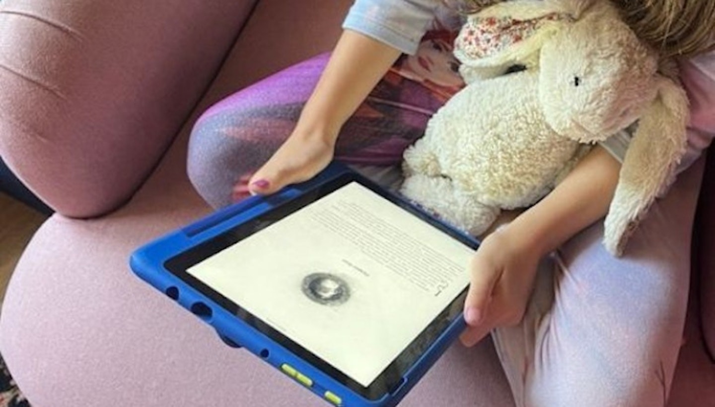 Child sitting in armchair with soft toy while using a tablet for kids