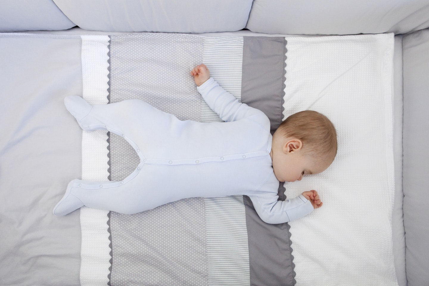 Eight months old baby boy sleeping in his little bed. He lie on his back in a blue pyjamas. This shows the best sleeping position for a baby with a stuffy nose.