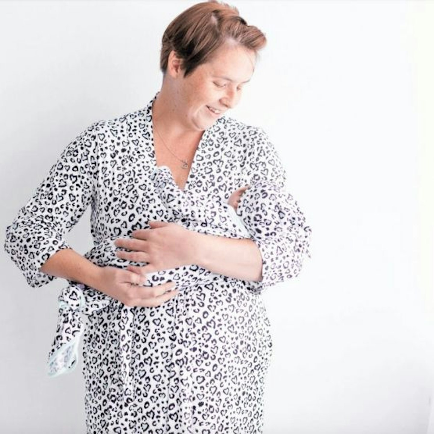 A woman wearing a mint leopard print maternity dressing gown and looking down at a baby wearing a matching sleepsuit 