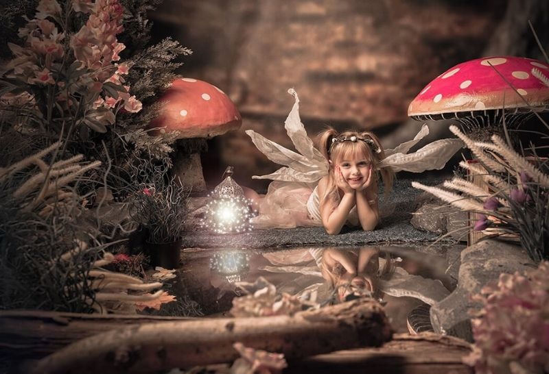 a girl dressed as a fairy in a woodland glade next two two toadstools