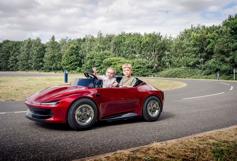 Two children driving a small red car around a track