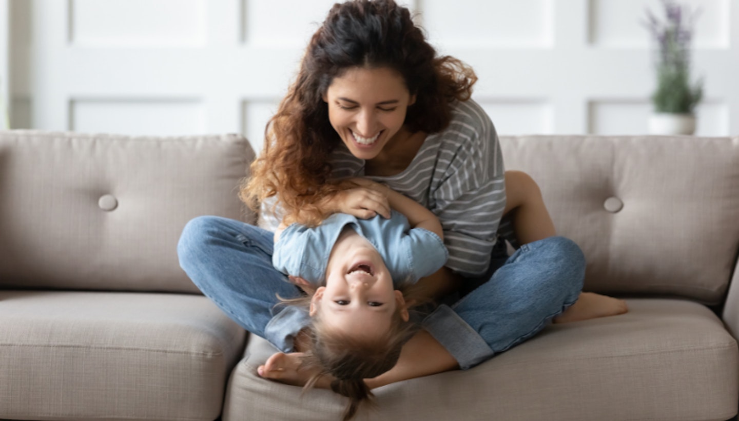 Happy young mother sit on couch in living room playing with excited little toddler