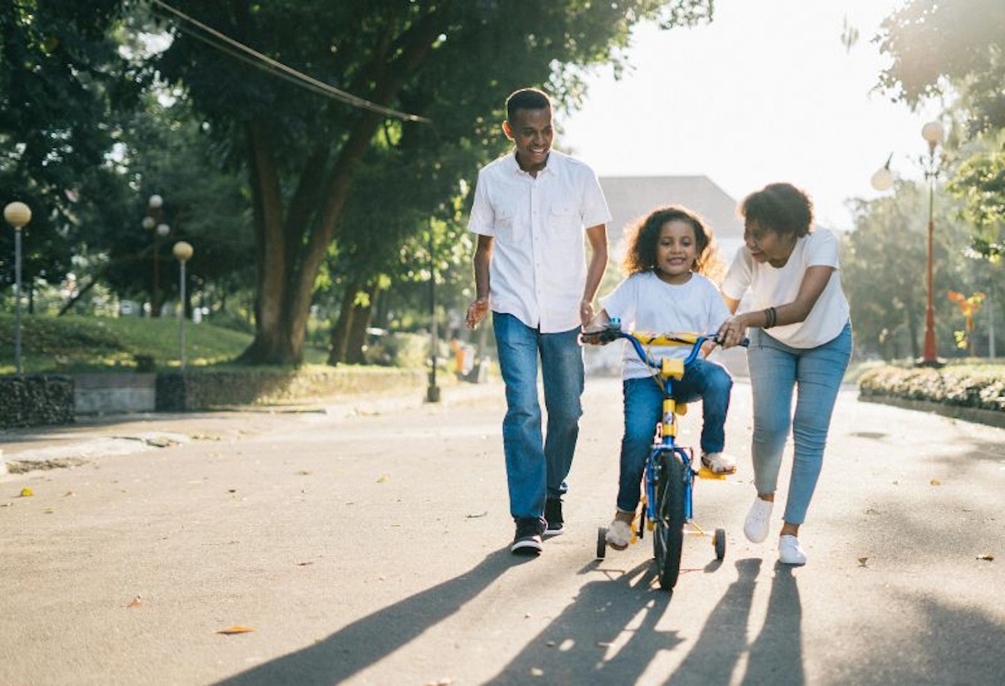 Adopted parents teaching their child how to ride a bike in a park