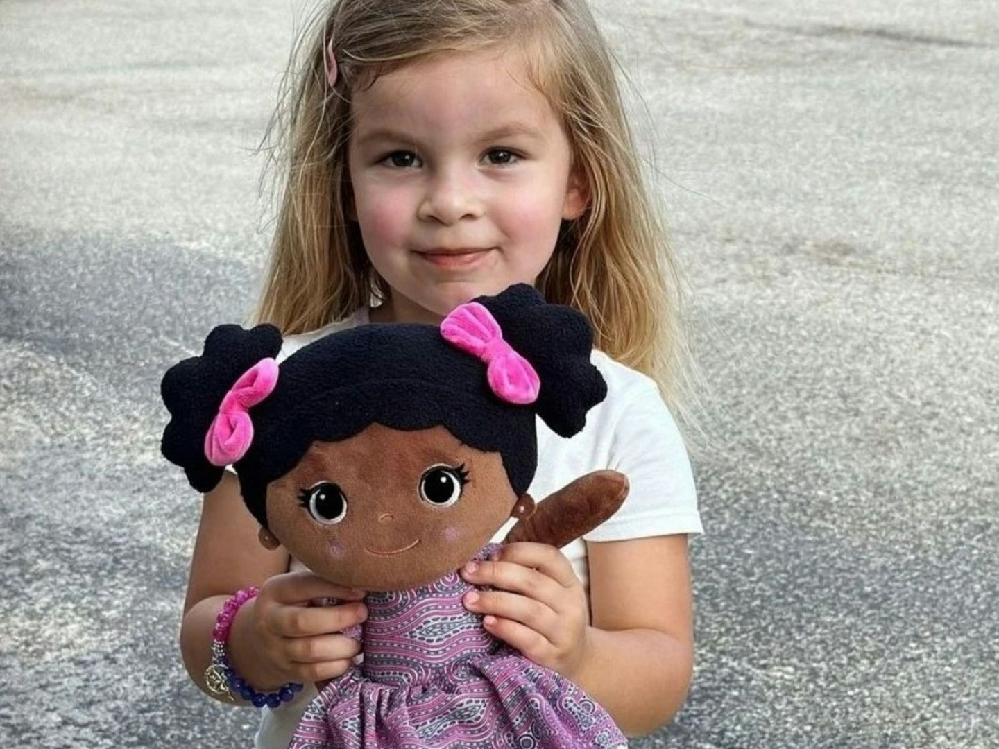 A young girl holds a Bibinee Doll in a pink and purple dress