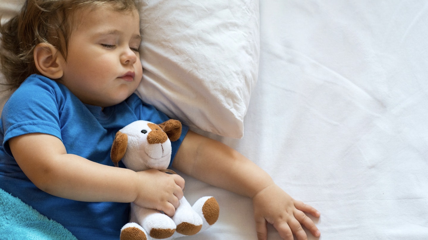Image of a little baby boy lying in bed hugging a cuddly toy