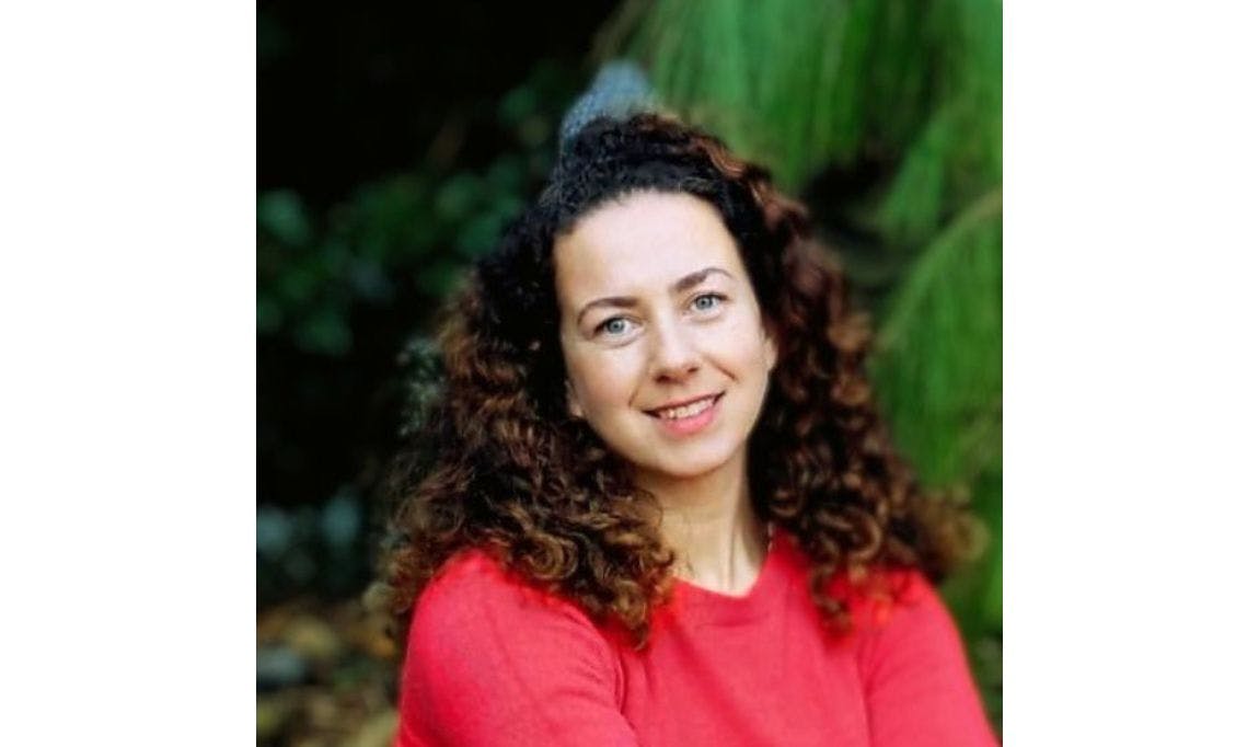 Dr Hazel Walklin wearing a red jumper in front of a green leafy background