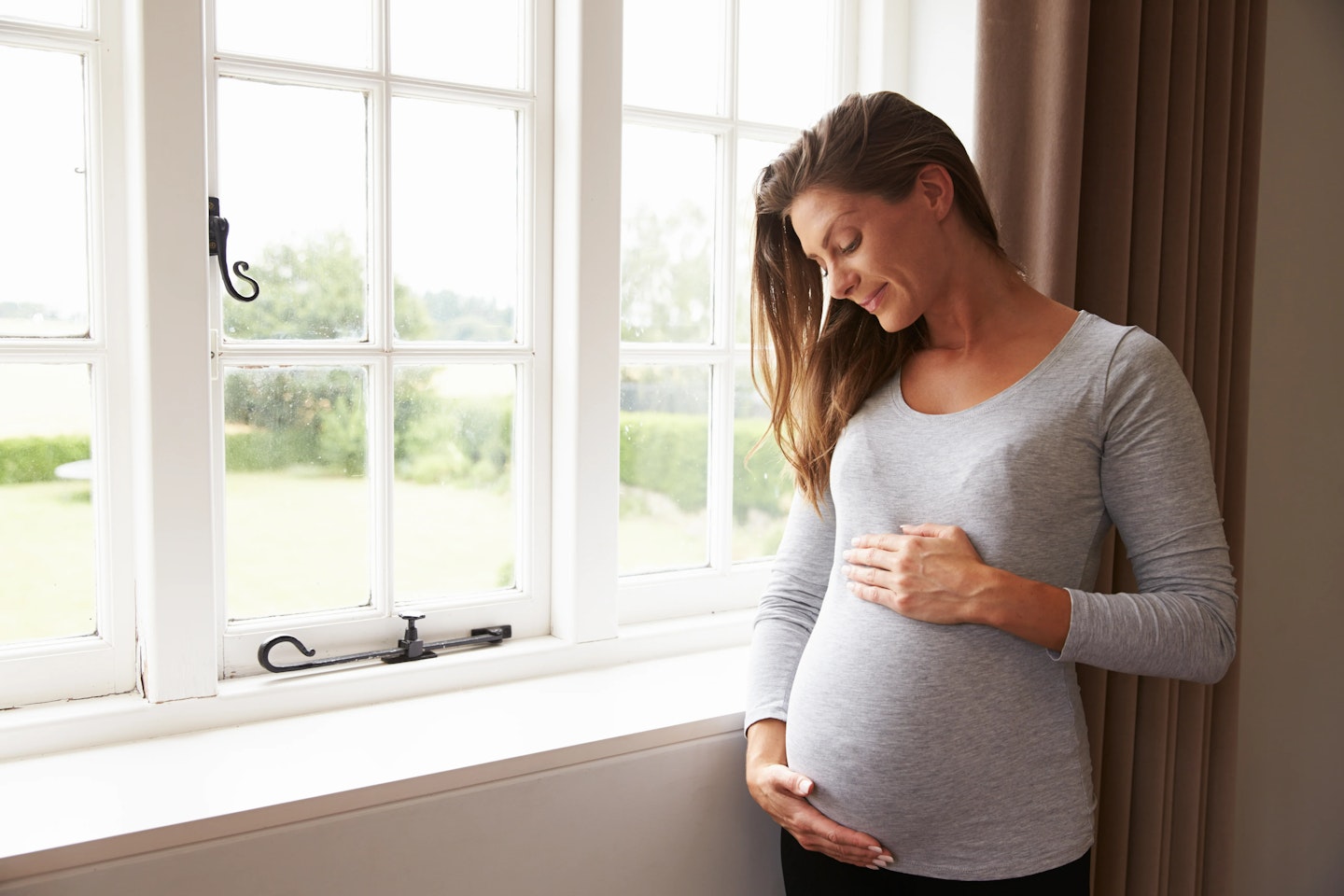 Woman holding pregnancy bump near window