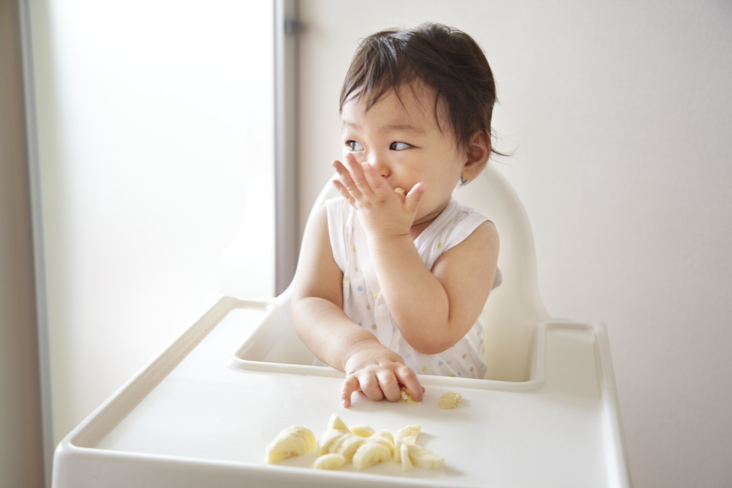 A baby boy eating banana in a high chair