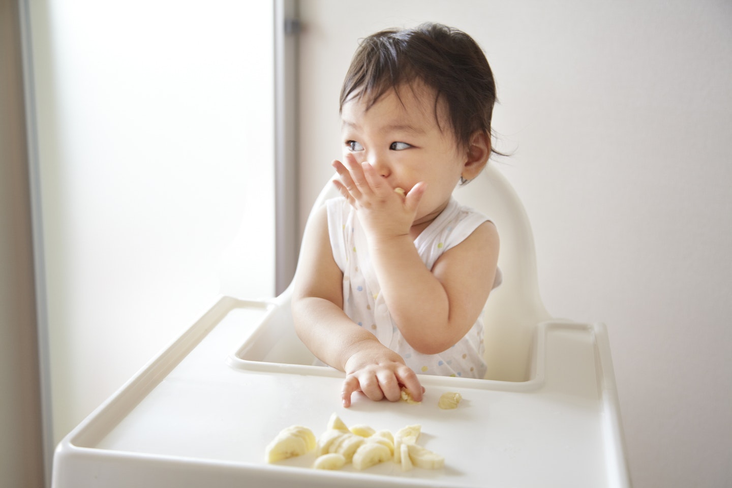 A baby boy eating banana in a high chair