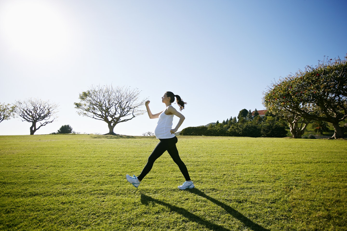pregnant woman walking across a park with trees in the background