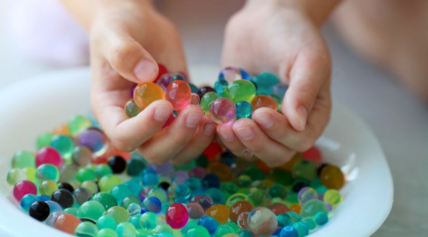 A close up of a child's hand scooping a handful of water beads from a bowl