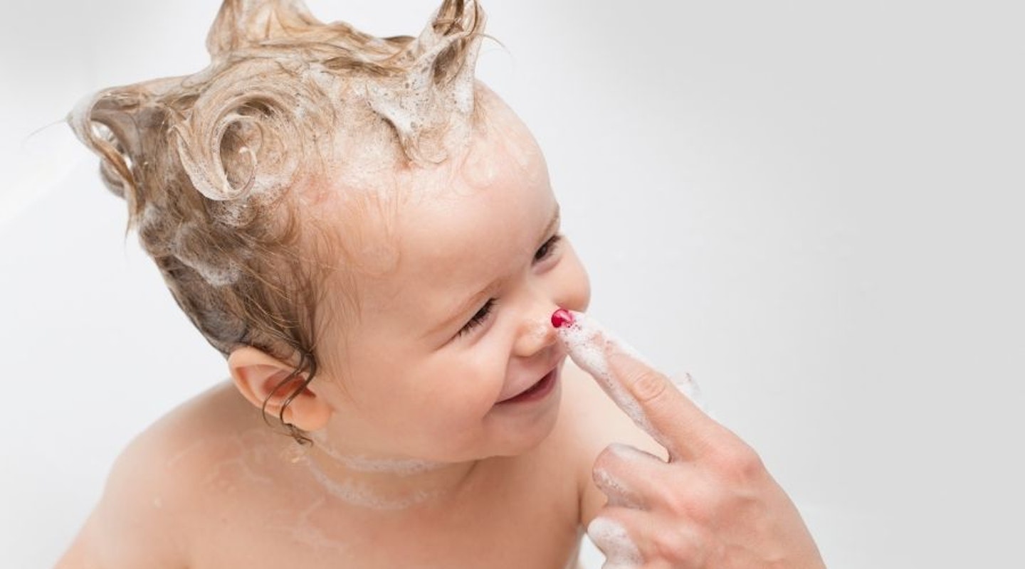A baby in the bath with baby shampoo in their hair.