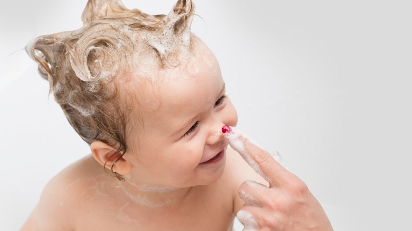 A baby in the bath with baby shampoo in their hair.