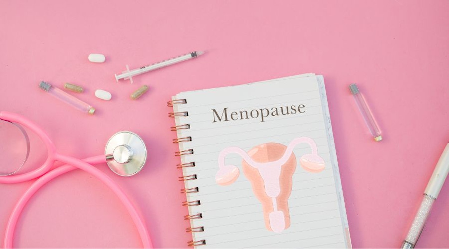 A notebook with the word menopause written on it and medical paraphernalia against a pink background