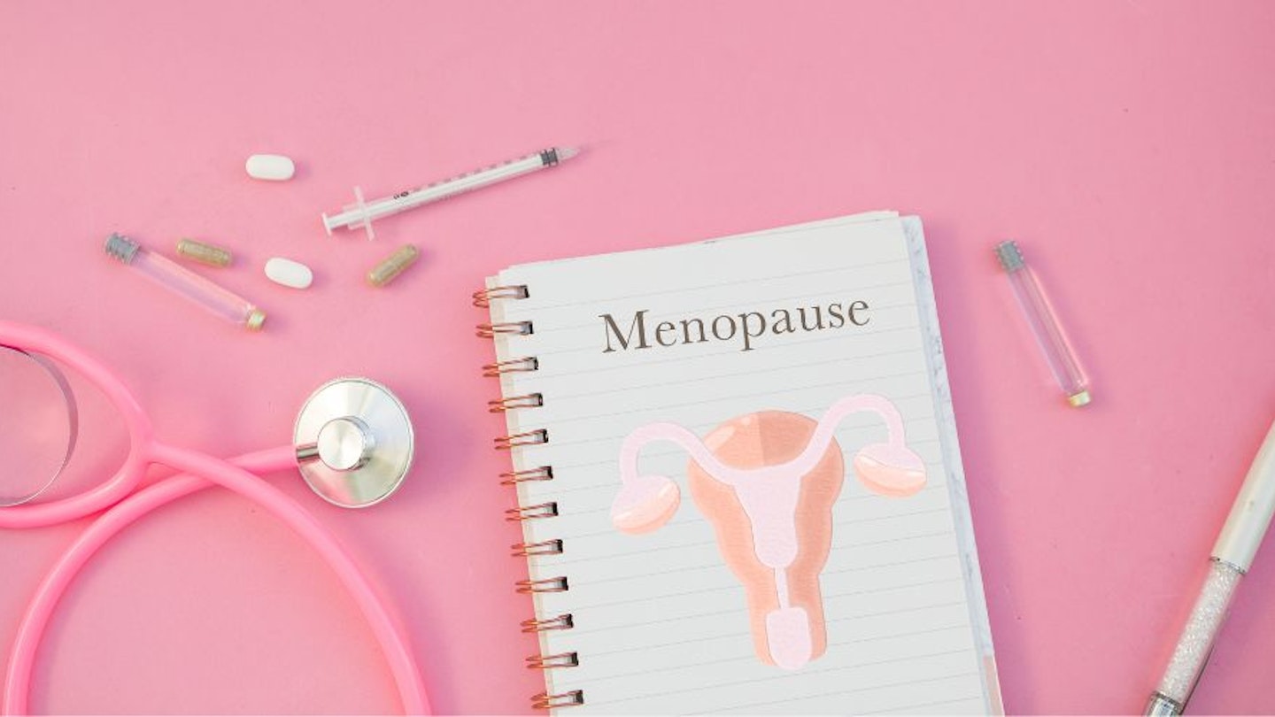 A notebook with the word menopause written on it and medical paraphernalia against a pink background