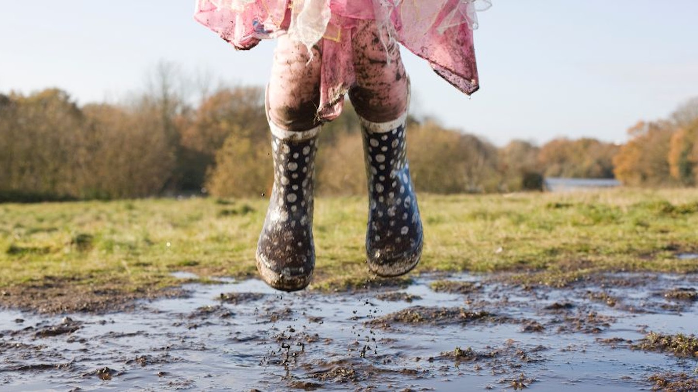 A toddler jumping in a puddle wearing wellies