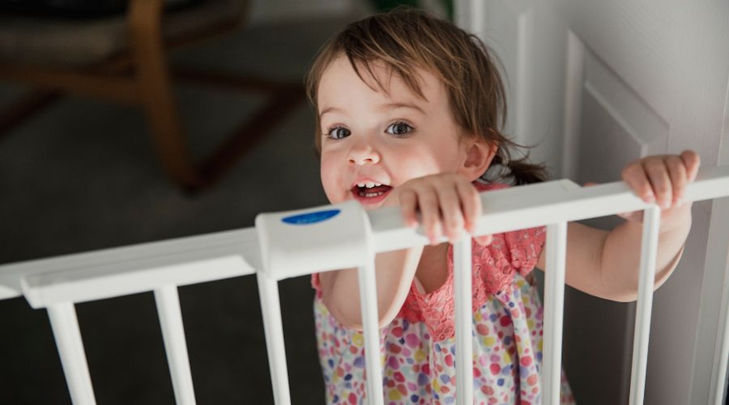 A baby holding onto a stair gate