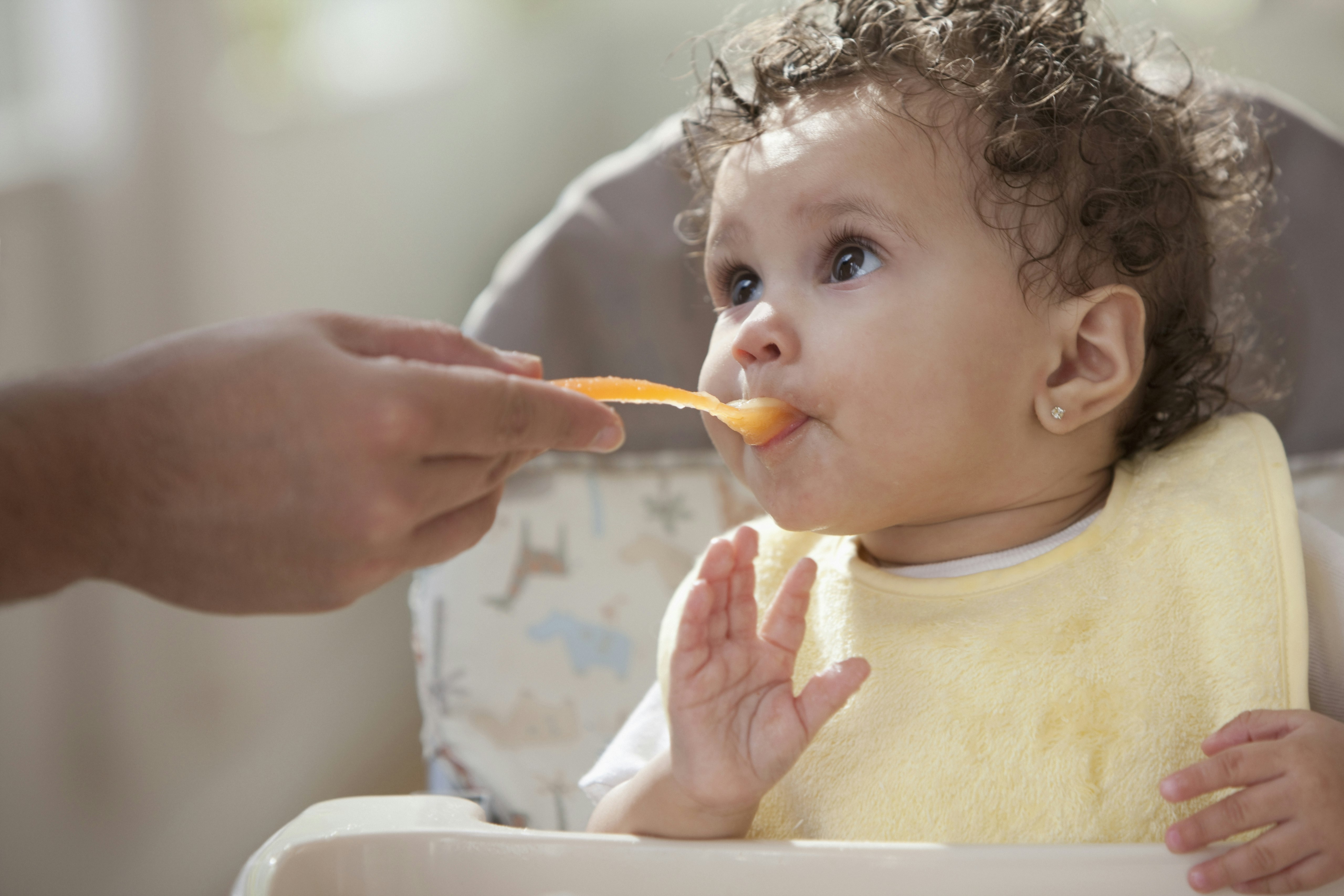 A baby sitting in a high chair and being spoon-feed