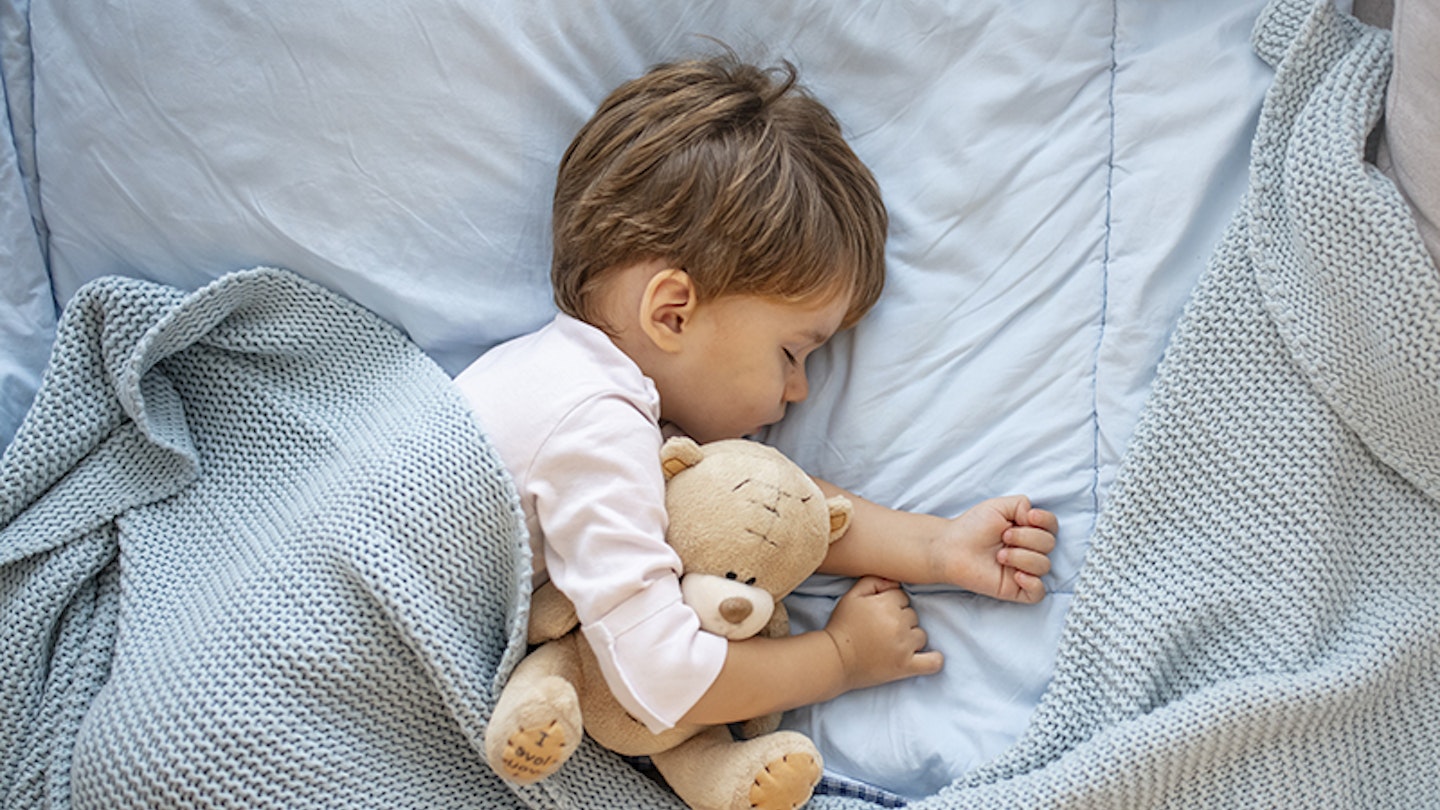 Toddler asleep in bed on a toddler mattress with teddy