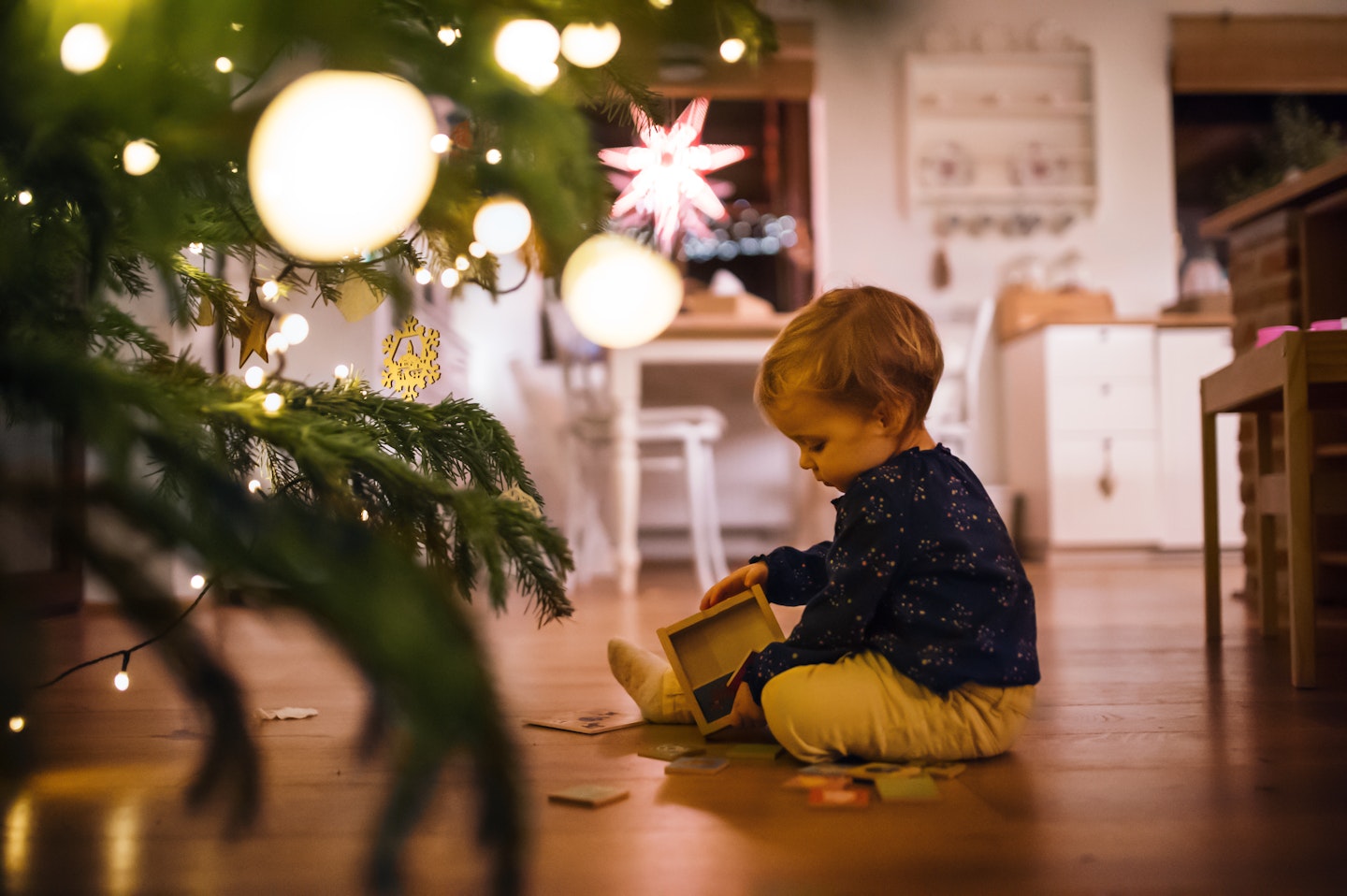 A toddler sitting near a Christmas tree playing with toys on his own