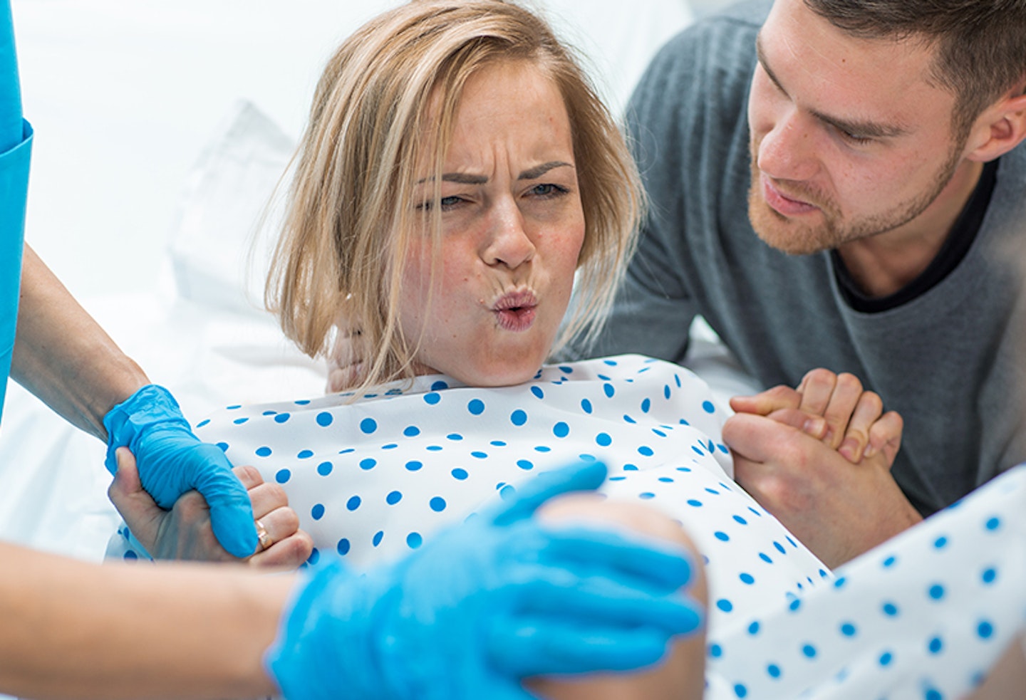 A woman giving birth in a hospital gown, with her birthing partner