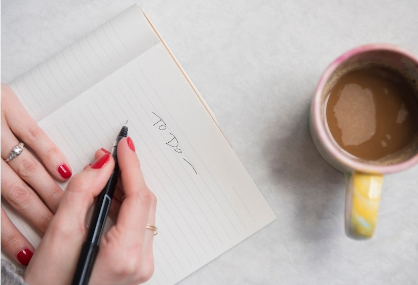 Birds-eye view of a woman's hand writing a to-do list with a coffee mug on the table