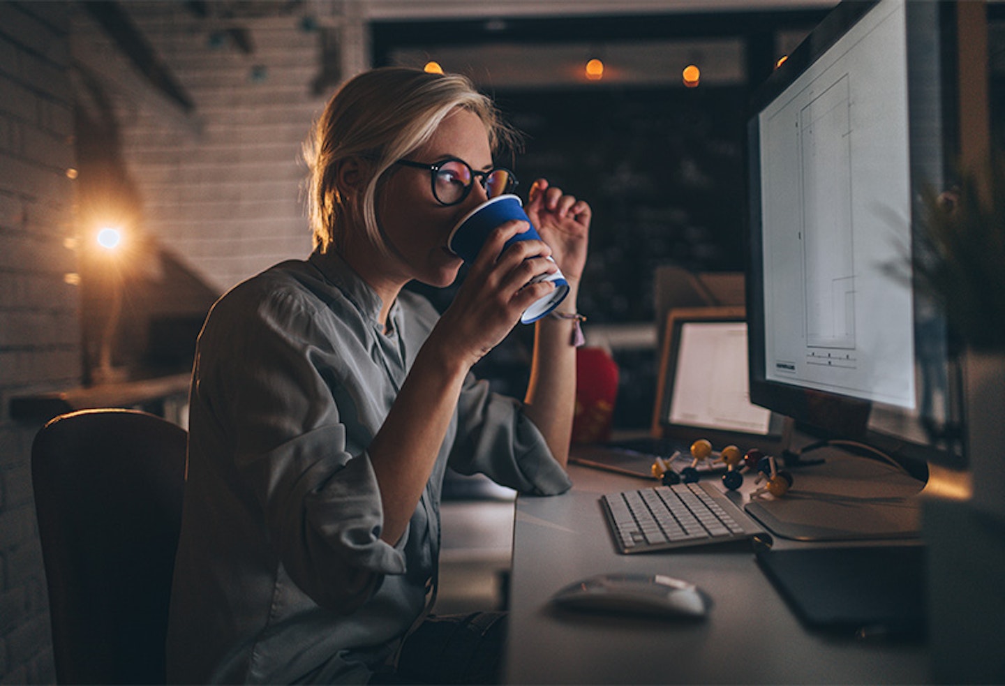 Woman drinking coffee is working late at her computer