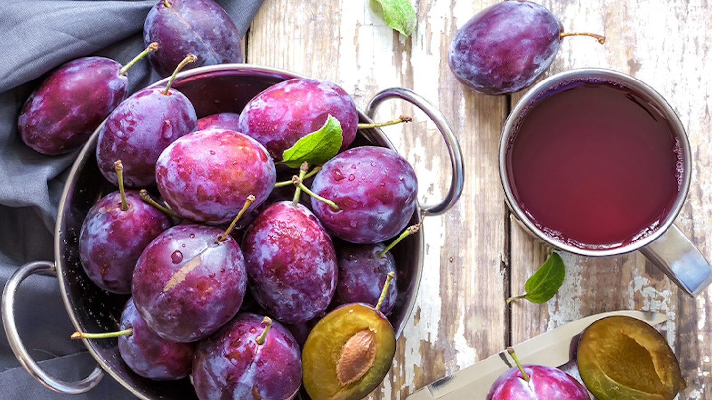 Rustic still life of fresh plums and a mug of plum/prune juice on a wooden surface