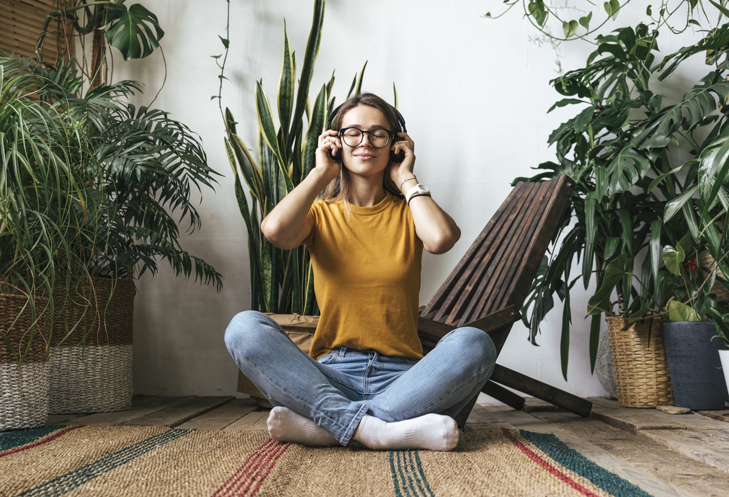 A mum sitting on the floor listening to music on headphones surrounded by green plants