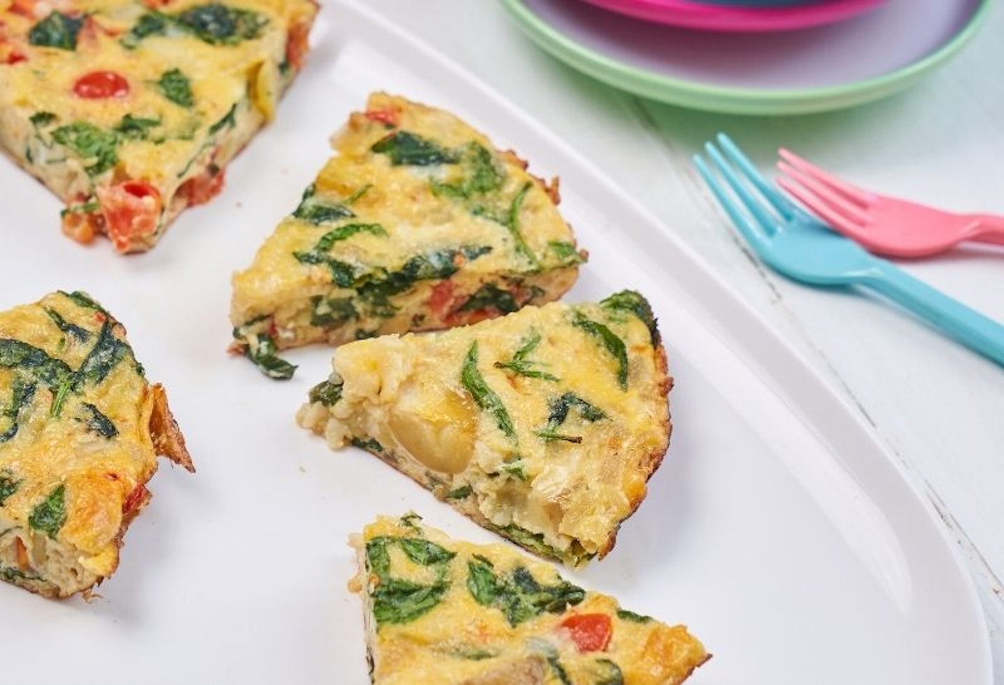 Slices of spinach and tomato frittata on a white plate