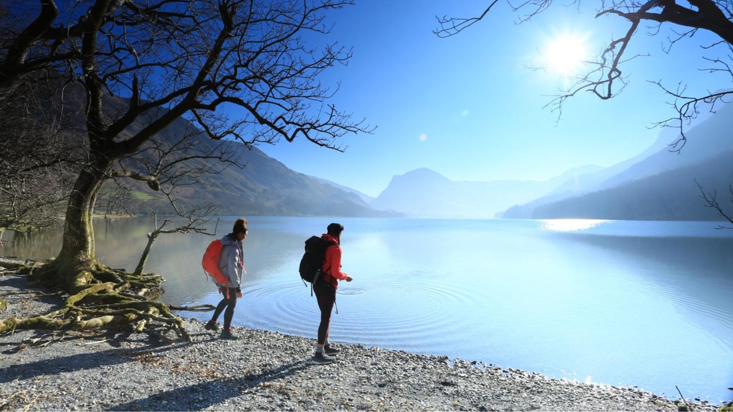 Hikers skimming stones into Buttermere with Fleetwith Pike beyond