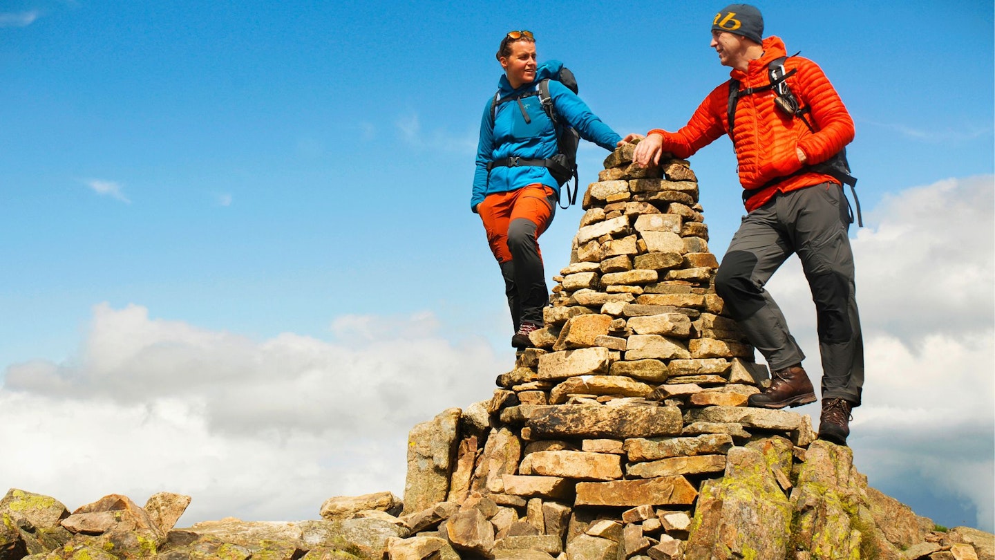Two hikers standing on a summit cairn wearing synthetic insulated jackets