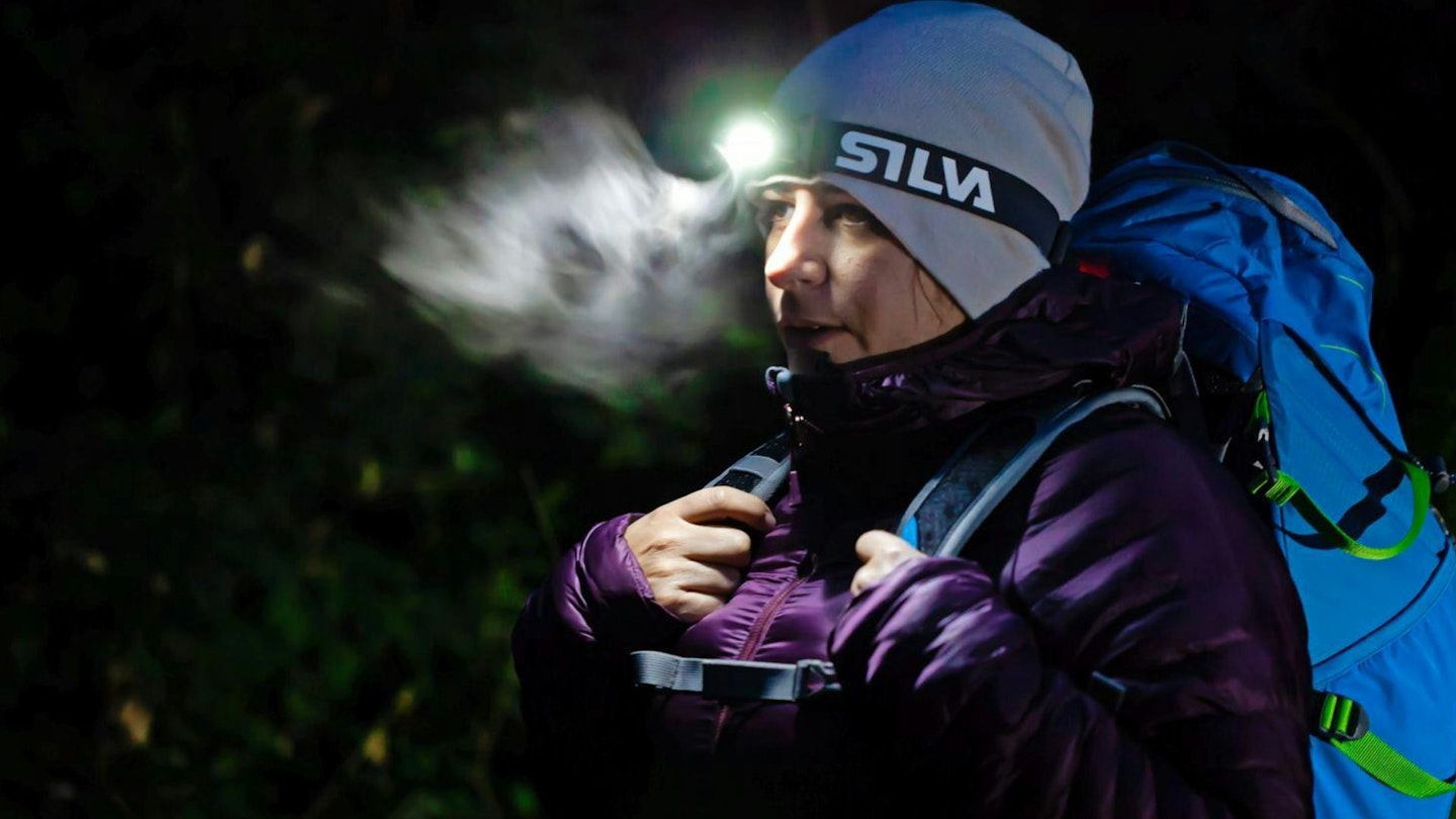 woman in winter at night breath illuminated by headtorch