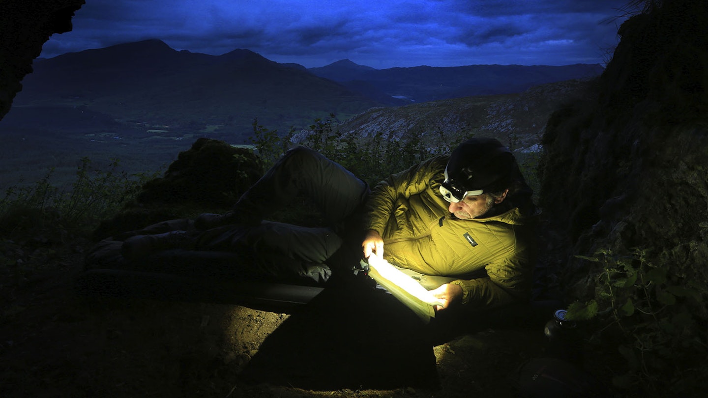 Reading with a head torch at dusk at Owain Glyndwr's Cave, Moel y Ogof with Snowdon in the distance