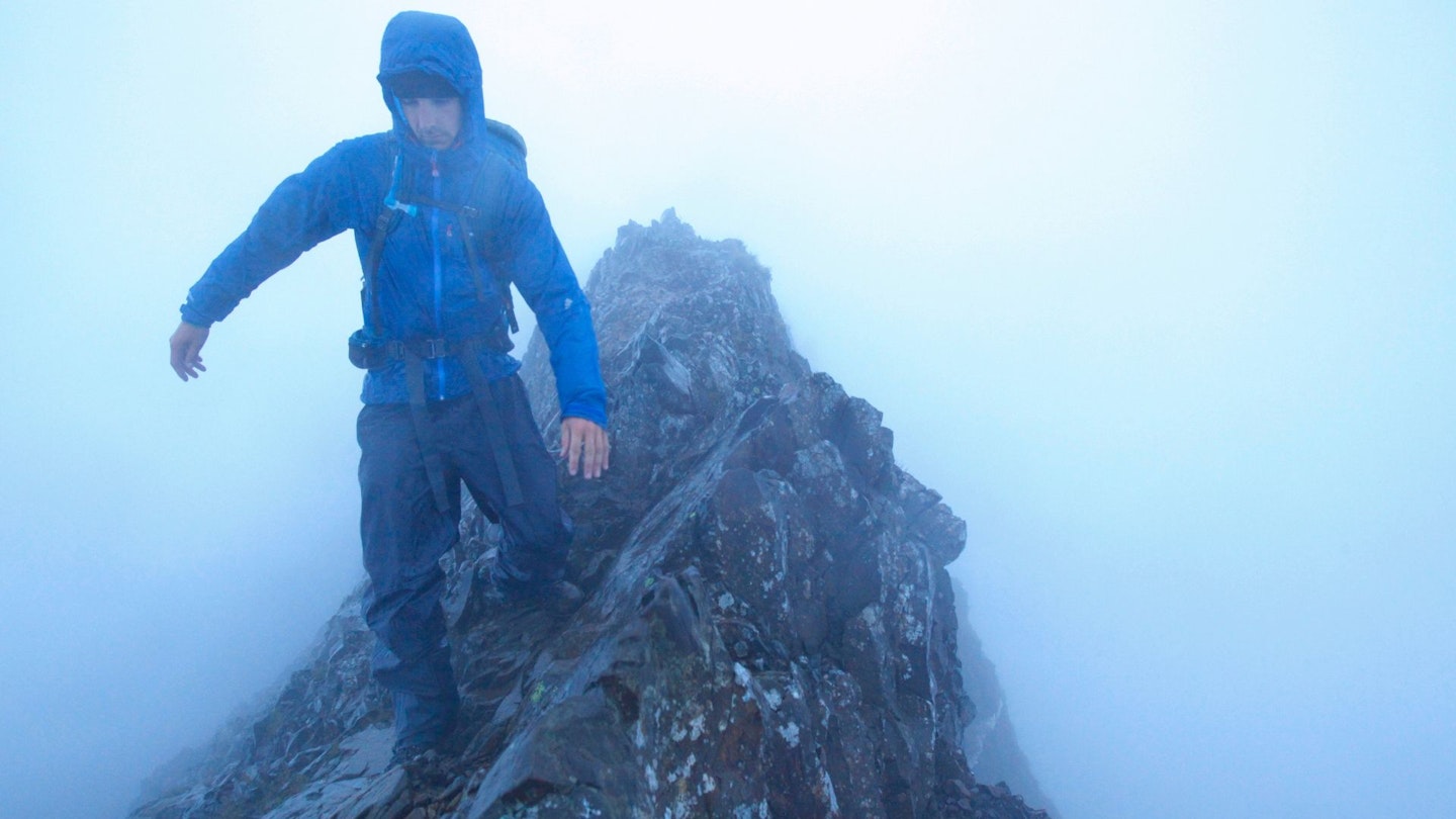 Hiker wearing waterproof clothing walking across a ridge in the mist