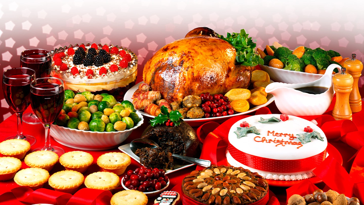 table filled with christmas foods like turkey, mince pies and cake