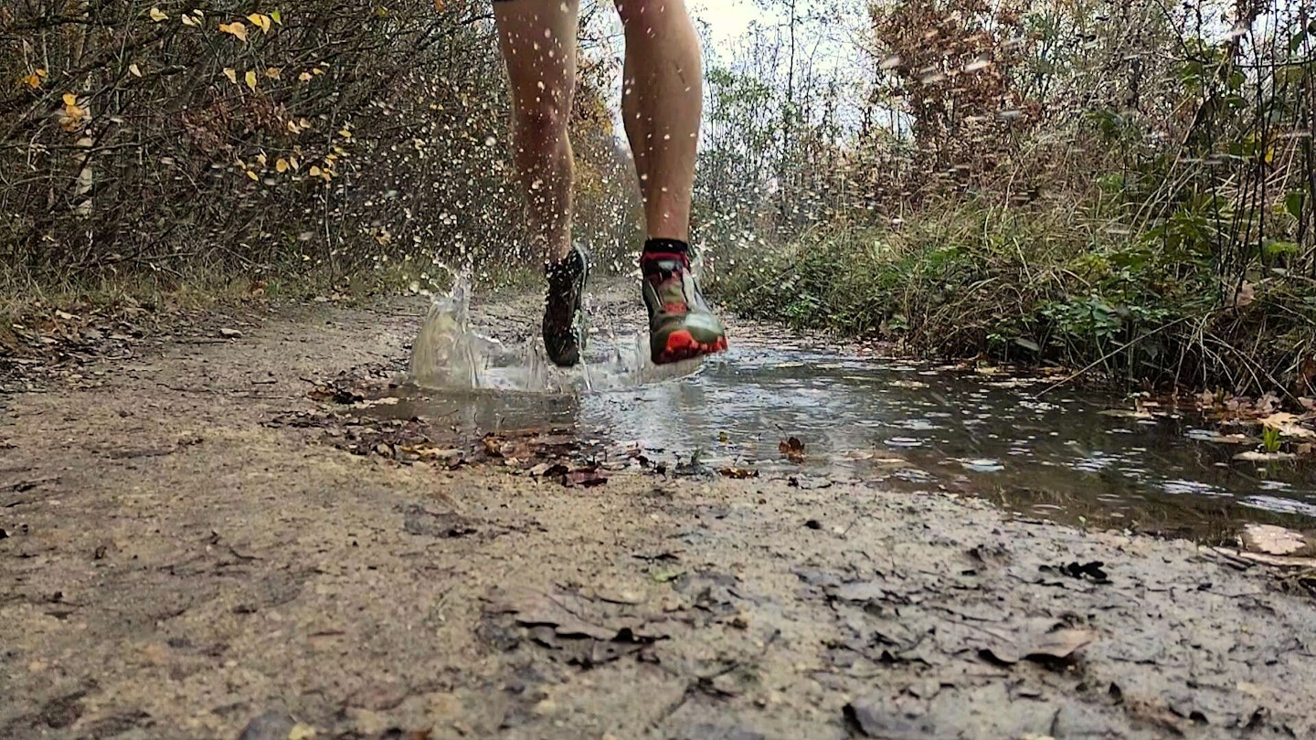 Closeup of runner's waterproof trail running shoes going through a puddle
