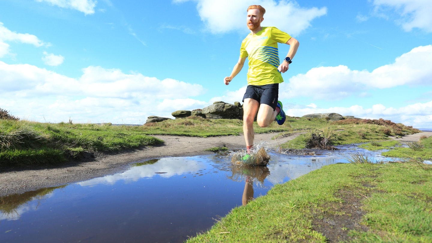 Trail runner going through a puddle on a dirt track