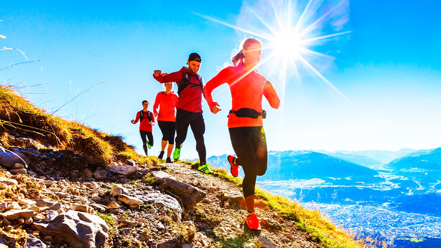 four runners run along a trail in the sun with packs and waist belts
