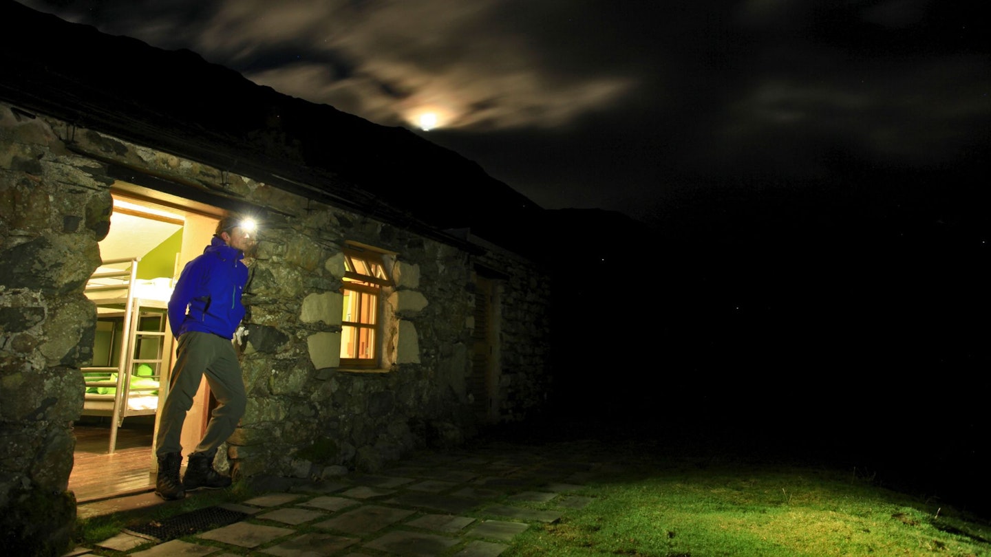 Hiker standing at door of YHA at night checking the weather