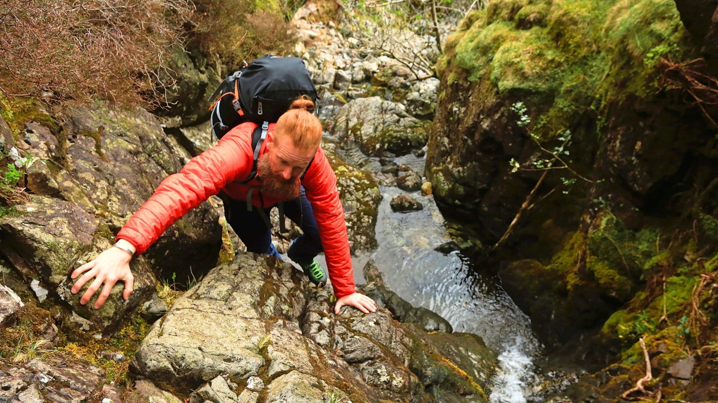 Hiker scrambling up a waterfall wearing a lightweight insulated jacket