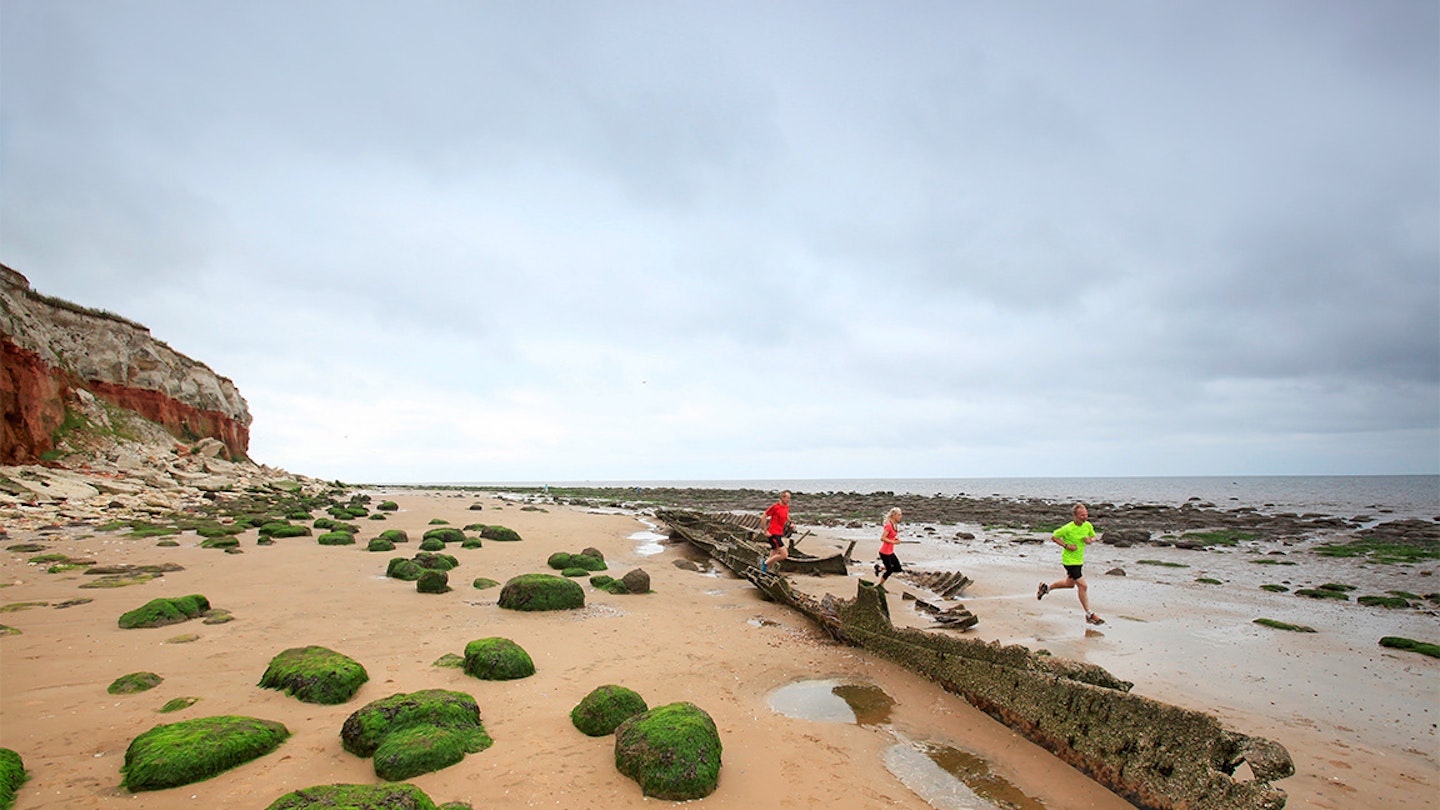 three runners run along a beach