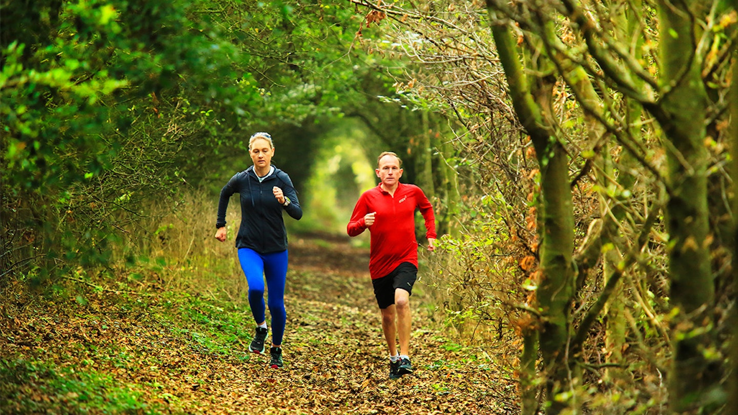 two runners sprint along a forest path
