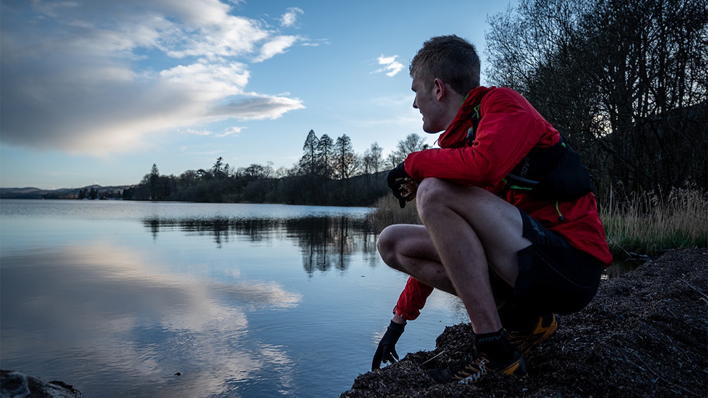 alex staniforth crouches down by a lake during a run