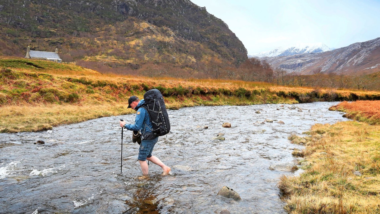Hiker wearing a large hiking backpack crossing a stream