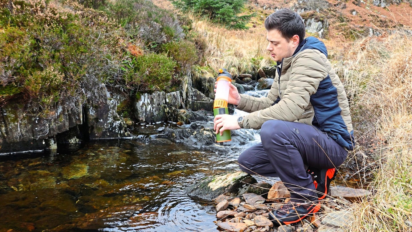 Hiker filling a drink bottle from a stream