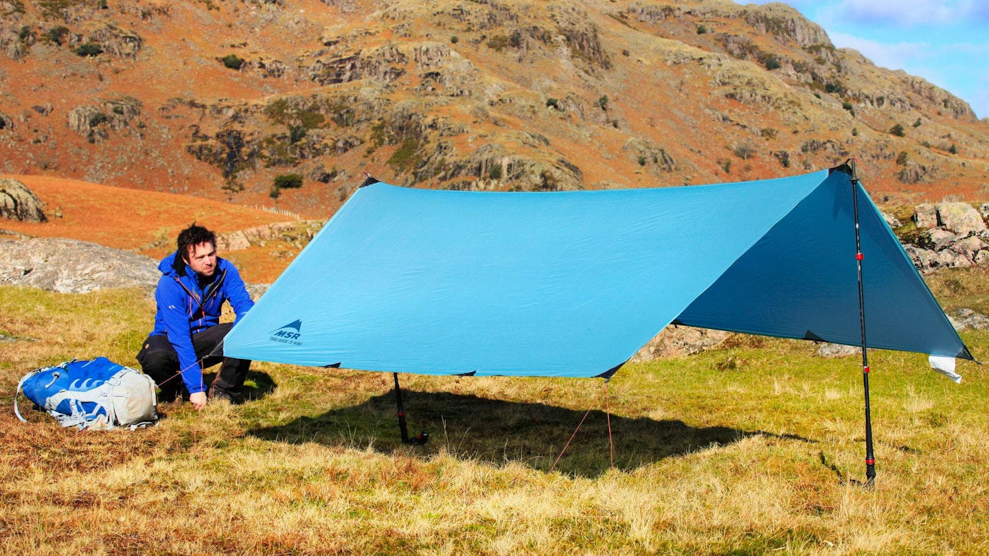 Hiker rigging a blue tarp