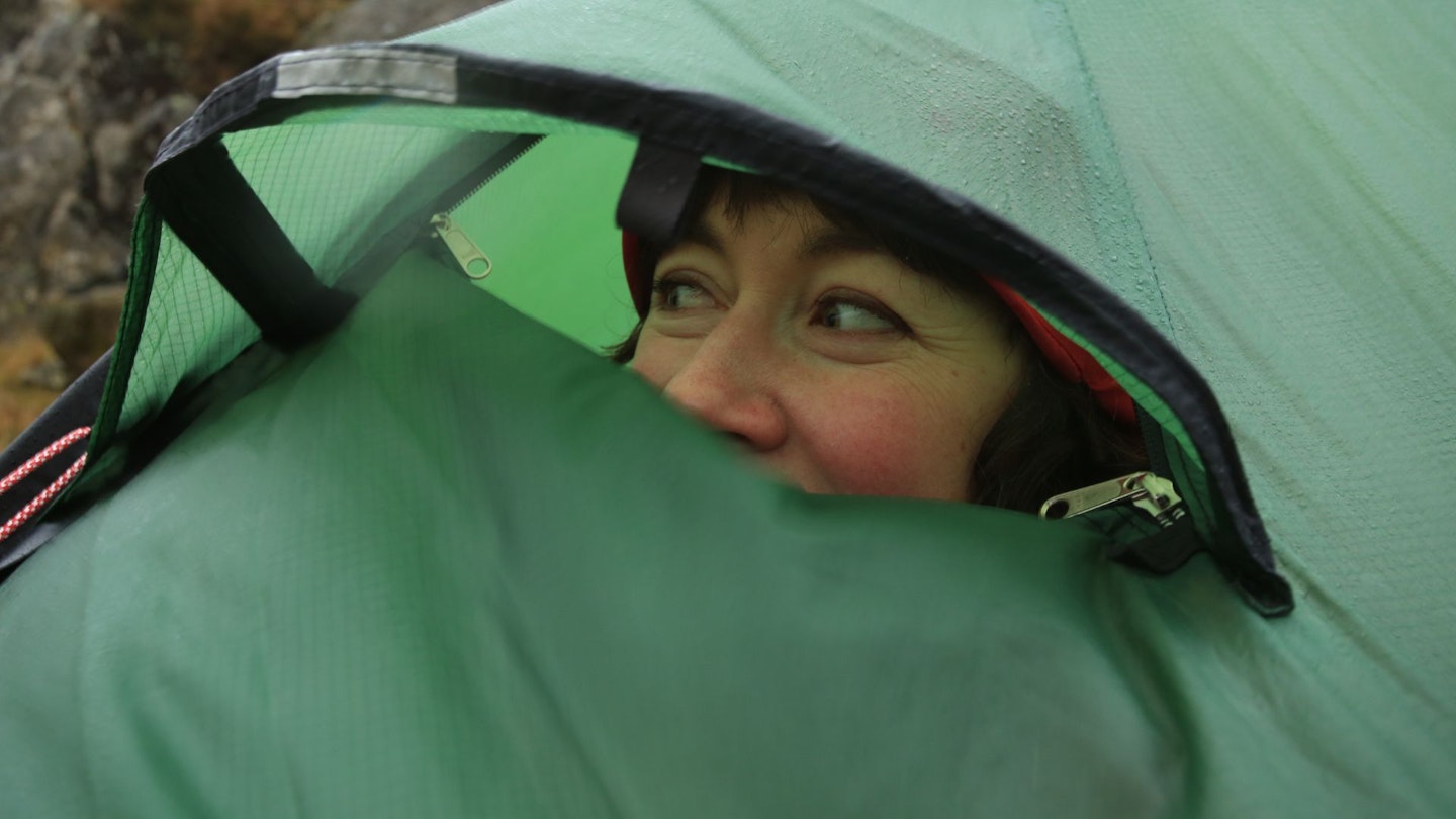 Hiker looking out from tent while raining