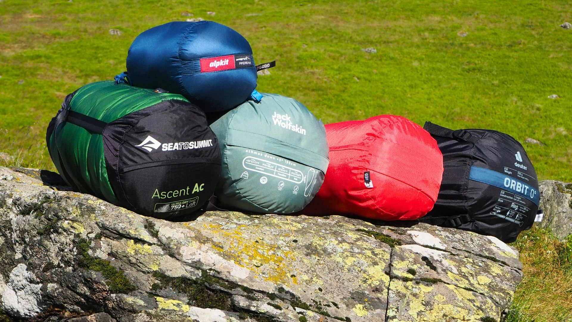 5 sleeping bags in compression sacks stacked on a rock