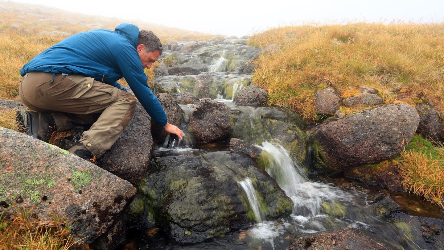 Filling a water bottle and filtering water from a stream on a hike